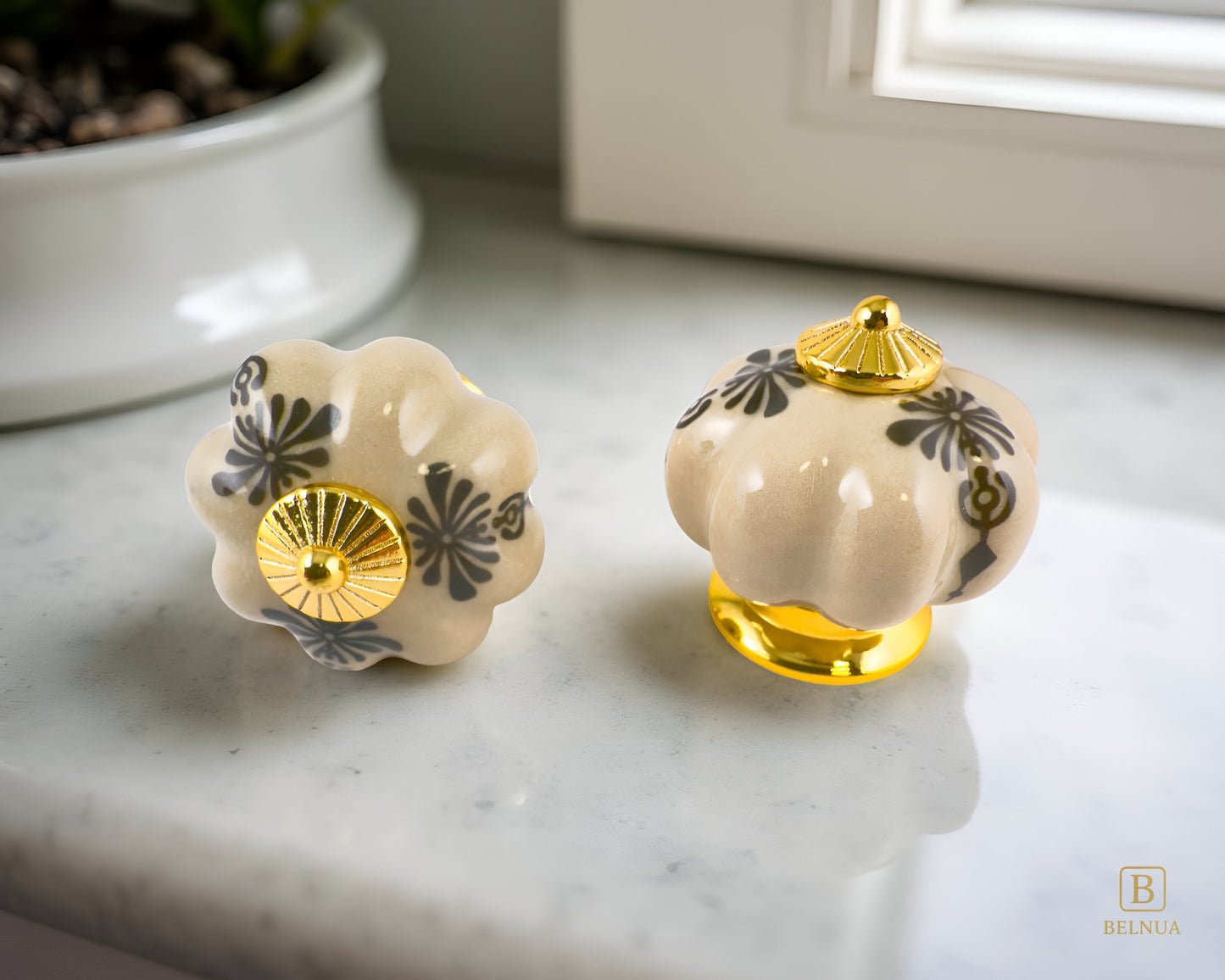 Belnua - Pair of Tavira antique brown cabinet porcelain knob with gold base featuring golden regal wreath motif on kitchen worktop with window background