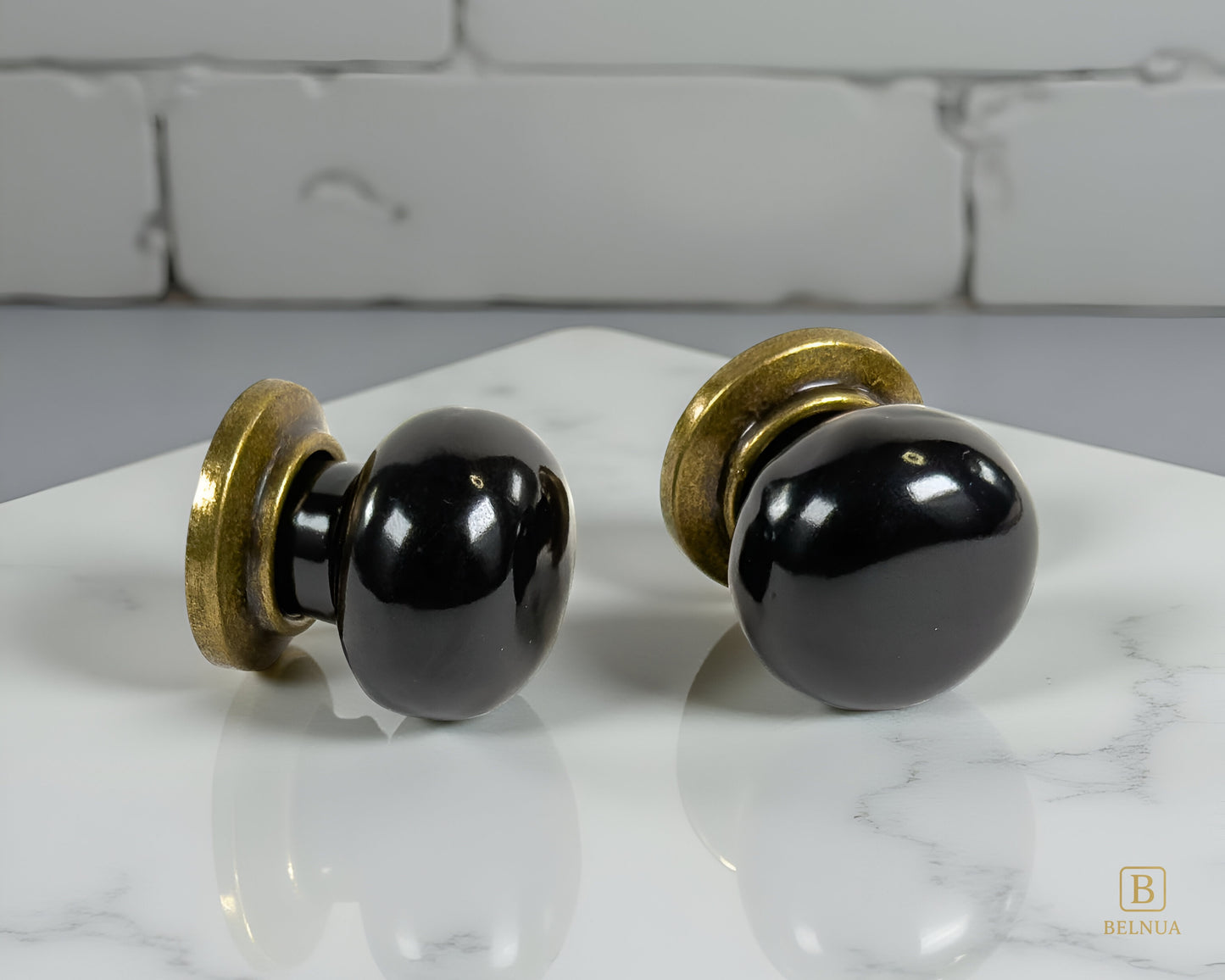 Pair of Zerra ceramic black cabinet knobs with brass hardware on a marble surface | Belnua