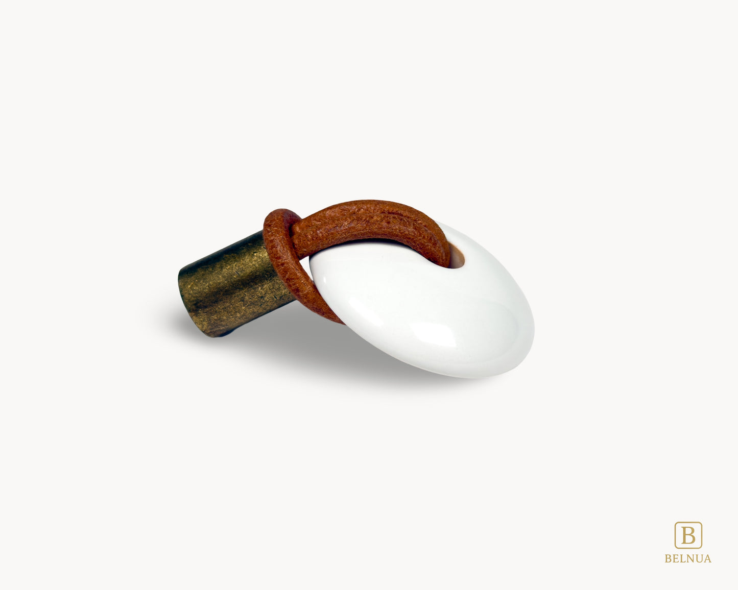 A single kitchen drawer pull made of white porcelain and antique brass with a sturdy leather loop handle.