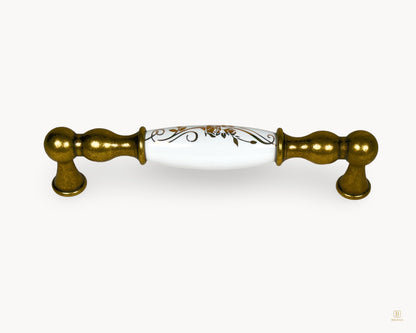 Belmira antique brass cabinet handle with white porcelain insert and golden scroll motif, 128mm centre to centre
