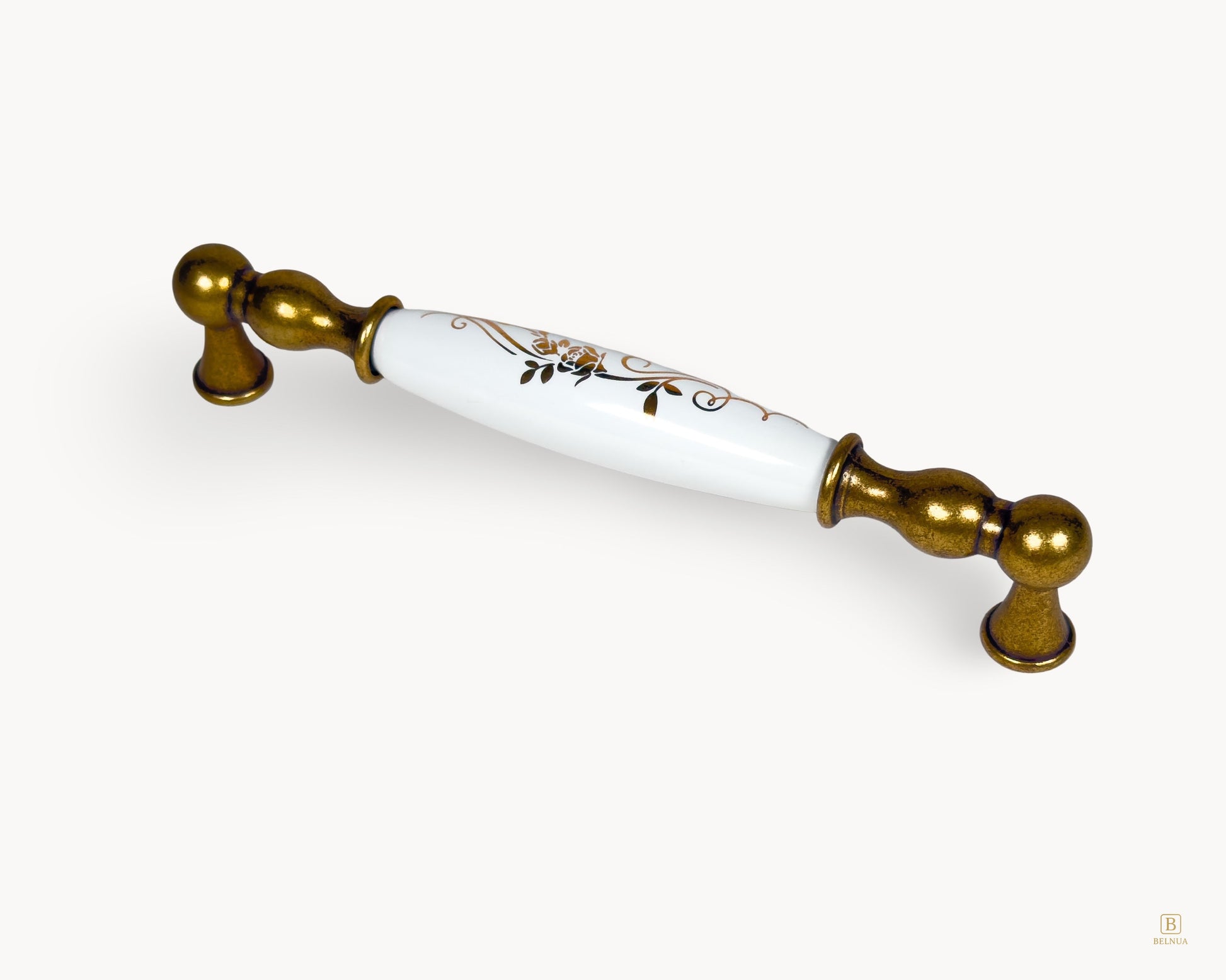 Angled view of Belnua Belmira antique brass cabinet handle with white porcelain and golden scroll motif, 160mm