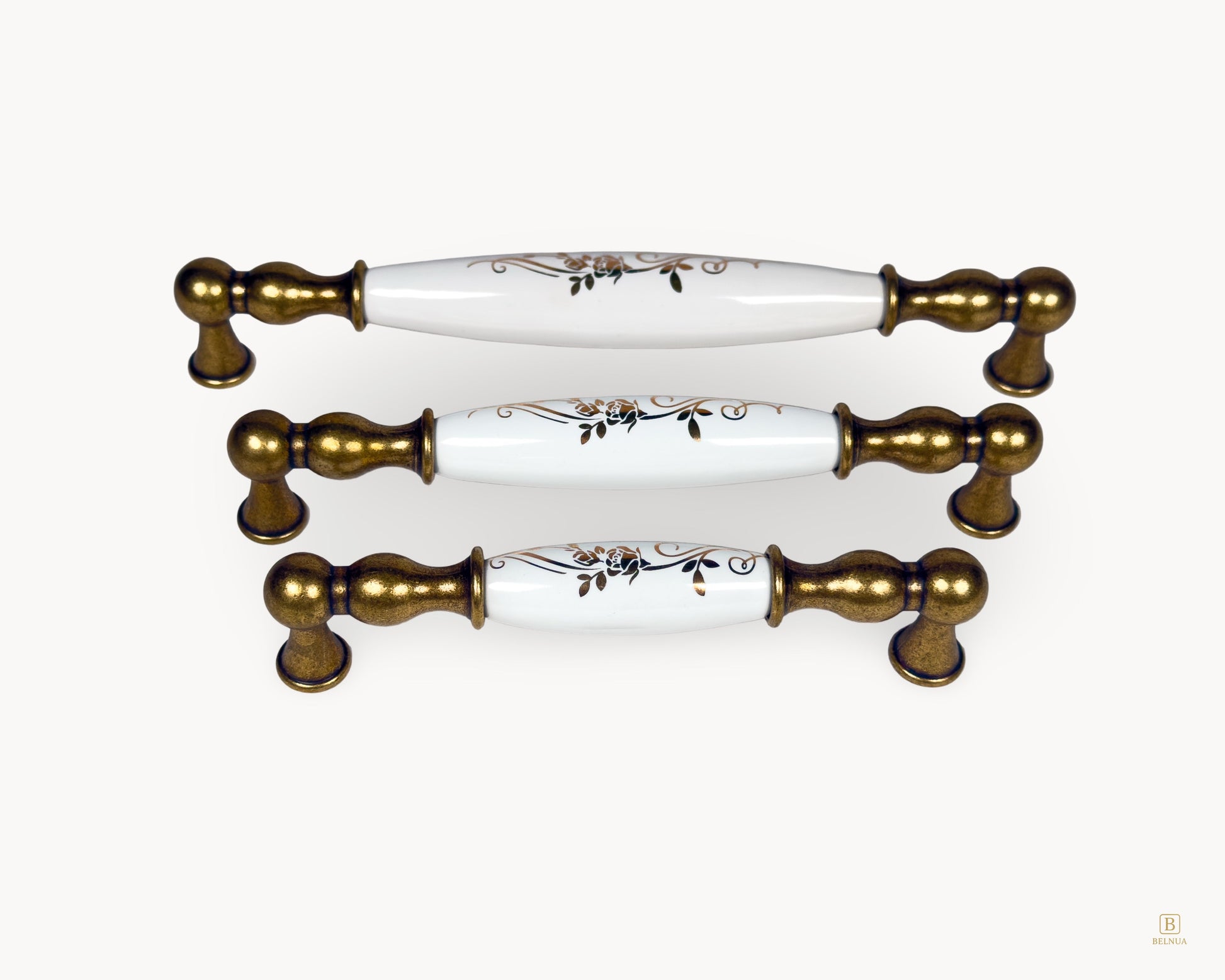 Front view of Belmira antique brass handles featuring white porcelain inserts with golden scroll pattern in three sizes