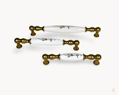 Styled group image of Belmira antique brass cabinet handles with white porcelain inserts and ornate golden scroll motif