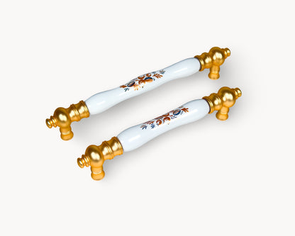Eloura gold cabinet handles with white porcelain insert and Golden Arch Bloom motif, luxury kitchen hardware shown in angled view