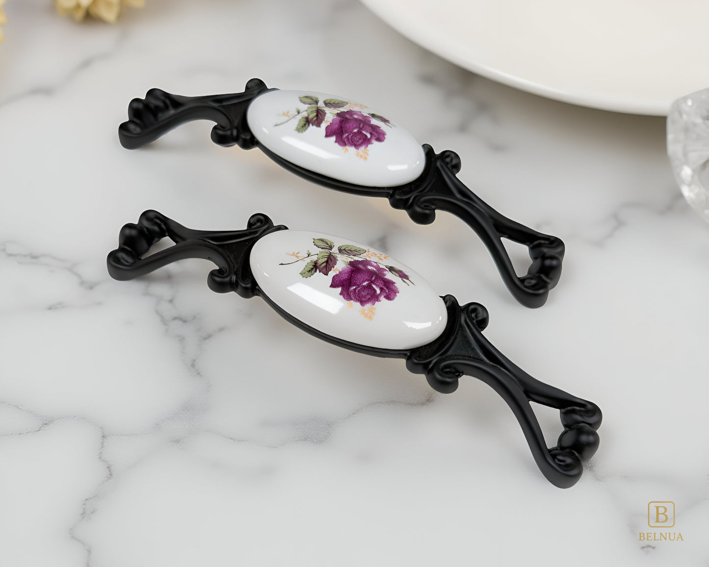 Belnua - Right angled view of Nureya cabinet pull handle with black metal base featuring rose motif on white ceramic/porcelain on white marble surface