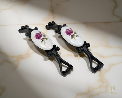 Belnua - Right angled view of Nureya cabinet pull handle with black metal base featuring rose motif on white ceramic/porcelain on crackle marble surface