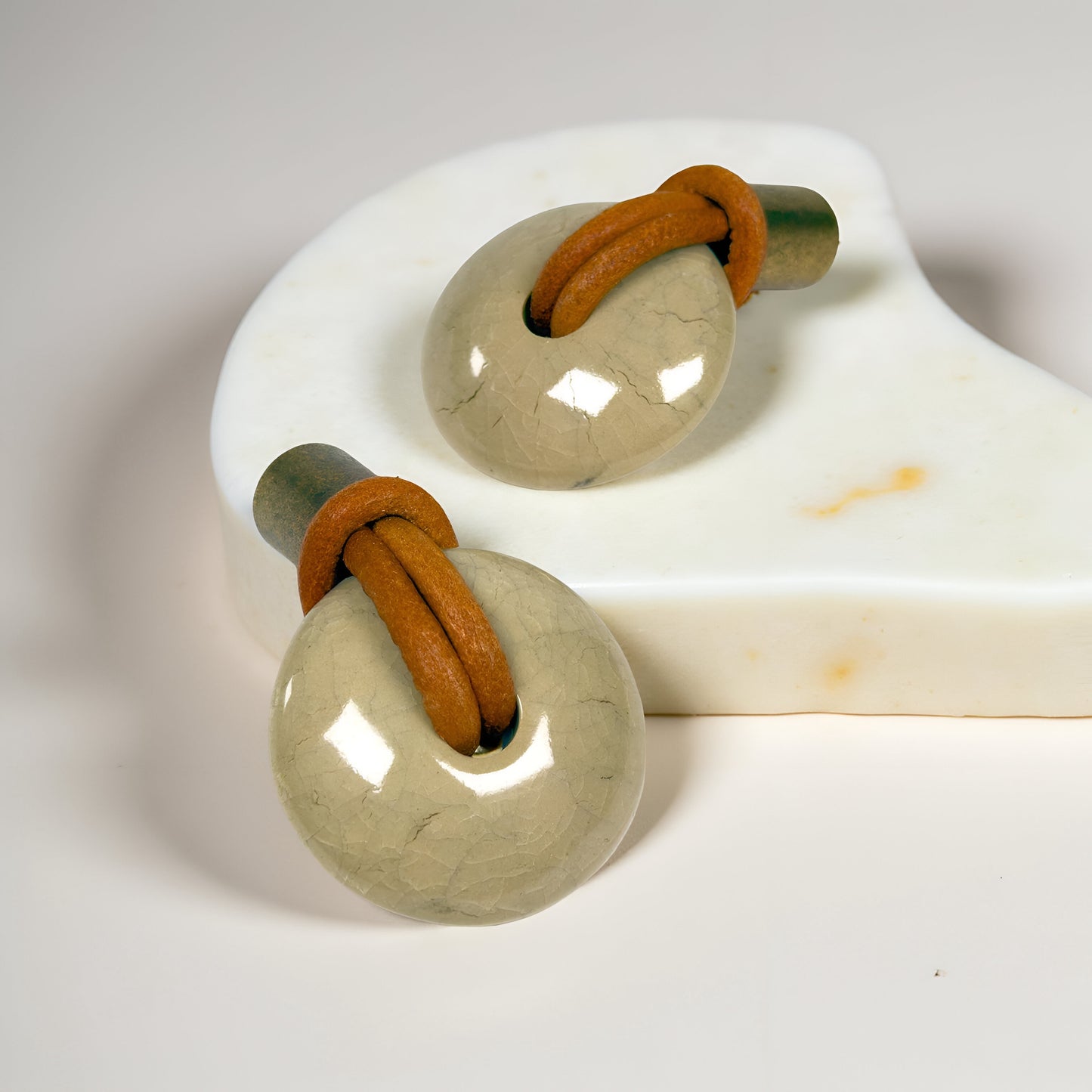 Angled view of REVINA porcelain knob highlighting curved ceramic surface and antique brass finish