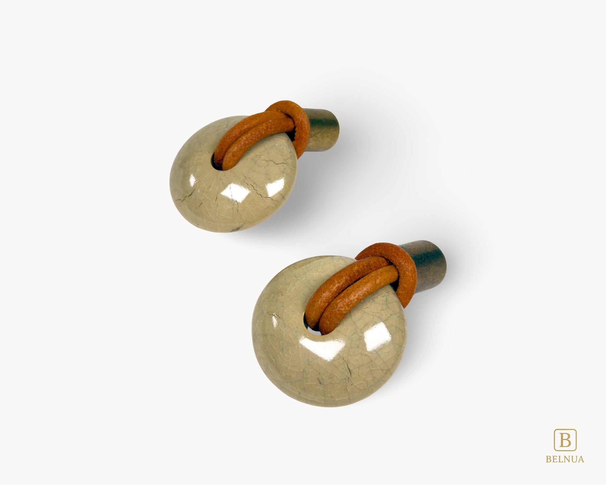 Pair of REVINA porcelain cabinet knobs with antique brass bases and leather loops on white background