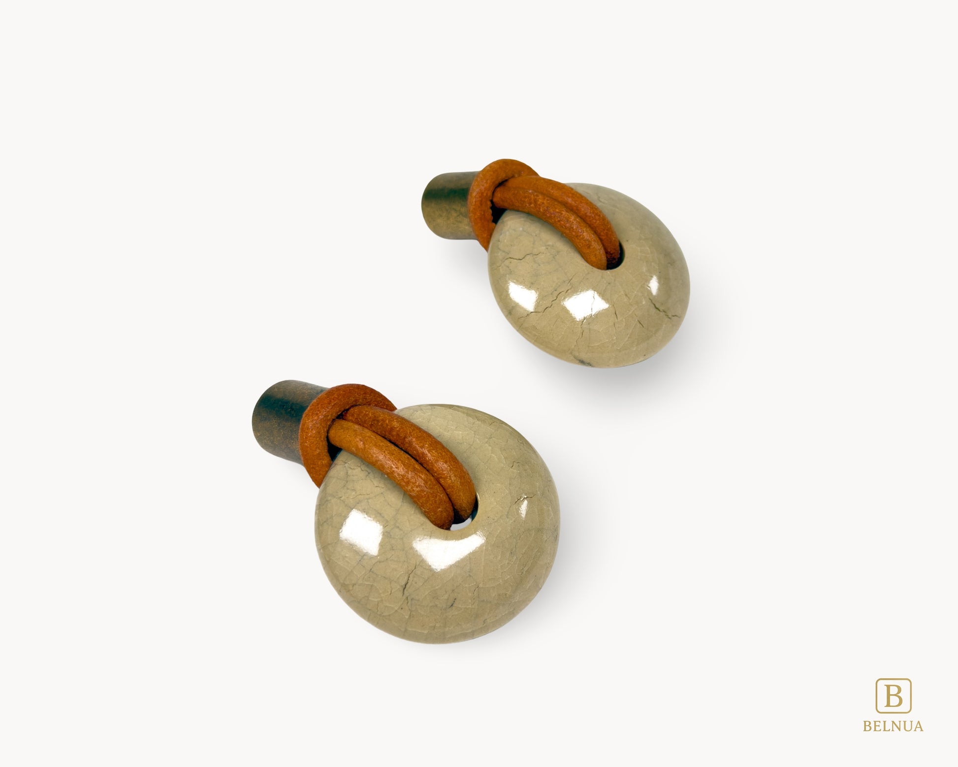 Two REVINA porcelain knobs arranged diagonally, showing ceramic texture and leather detailing