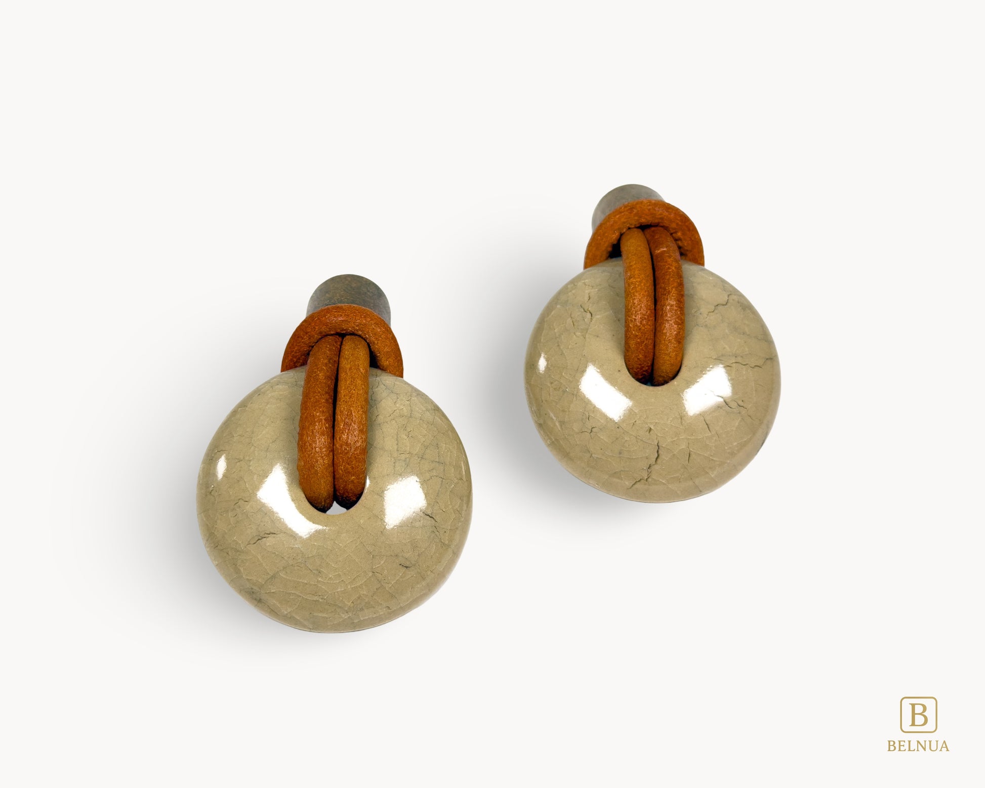 Symmetrical pair of REVINA porcelain knobs with leather loops and antique brass finish