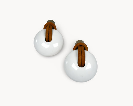 Front-facing view of two Belnua Revina white porcelain knobs with antique brass accents and leather pulls.