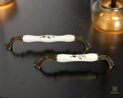 Belnua - ROSMIRA white porcelain/ceramic handle with earth motif and antique brass finish on black surface with light