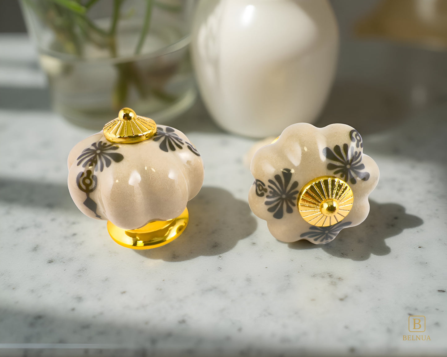 Belnua - Tavira gold base antique brown cabinet porcelain knob with golden regal wreath motif on marble worktop and floral background