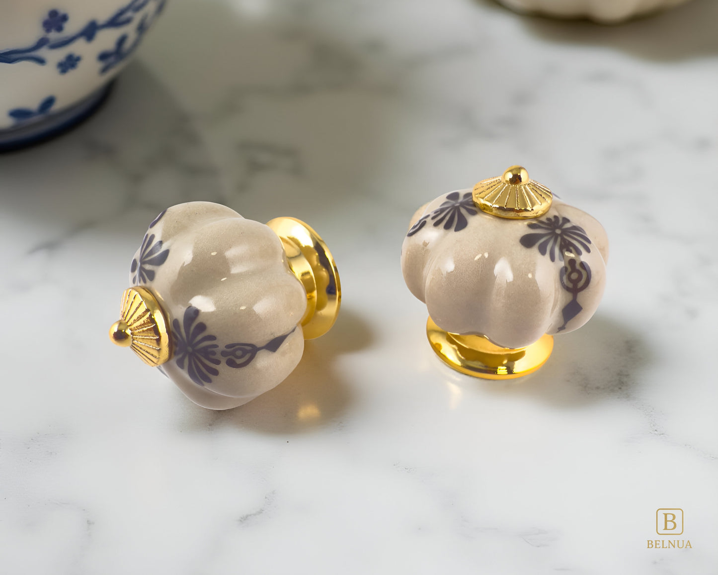 Belnua - Top and side view of Tavira antique brown cabinet porcelain knob with gold base featuring golden regal wreath motif on marble/quartz surface. 