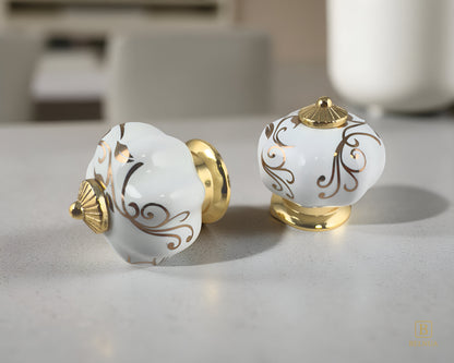 Belnua - Top and right side closeup view of luxury Tavira white porcelain cabinet knob with gold metal base on beige surface