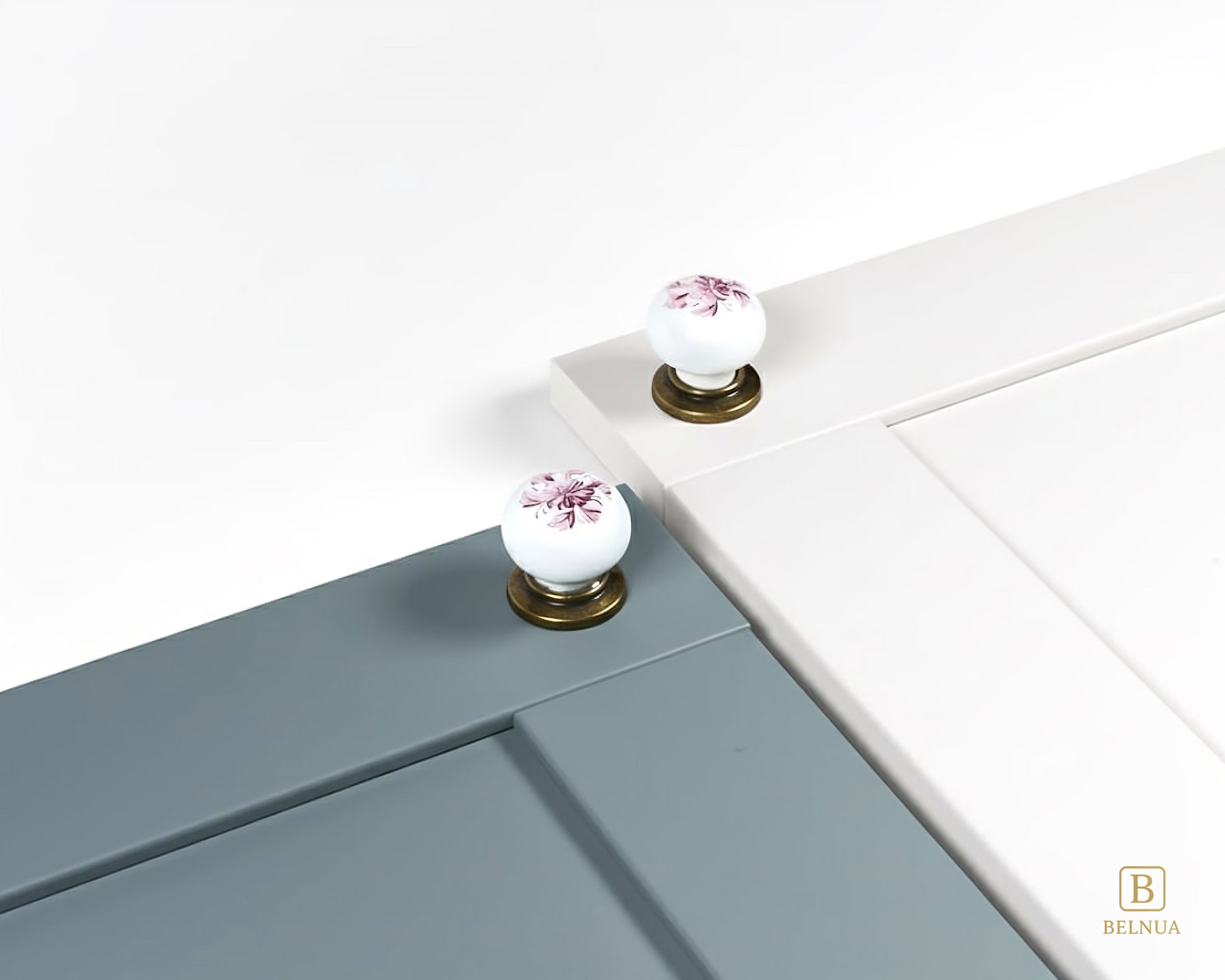 Belnua - Close up top view of ZERRA white porcelain/ceramic knob pair with antique brass base featuring with dusty blue and white cabinet door