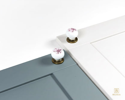 Belnua - Close up top view of ZERRA white porcelain/ceramic knob pair with antique brass base featuring with dusty blue and white cabinet door