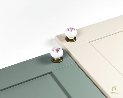 Belnua - Close up top view of ZERRA white porcelain/ceramic knob pair with antique brass base featuring with sage green and cream cabinet door