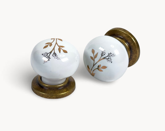 Pair of Zerra white ceramic cabiet knobs with floral design and brass bases on a white background | Belnua