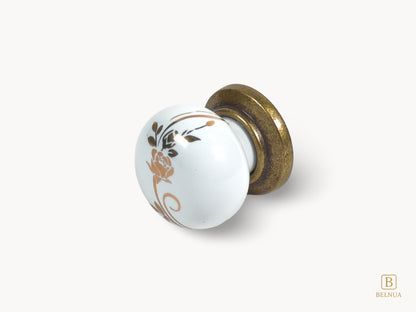 Belnua - Flat lay left view of ZERRA white ceramic/porcelain knob with golden scroll motif and antique brass base
