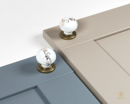 Belnua - ZERRA porcelain/ceramic white knob with golden scroll motif with antique brass base on dusty blue and light taupe cabinet door