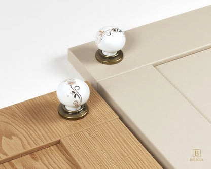 Belnua - ZERRA porcelain/ceramic white knob with golden scroll motif with antique brass base on oak wood grain and cream cabinet door