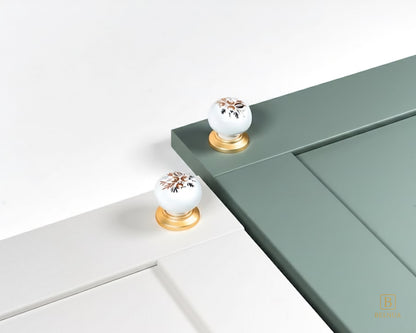 Belnua - ZERRA porcelain/ceramic white knob with golden arch bloom motif showcasing with dove grey and sage green cabinet door