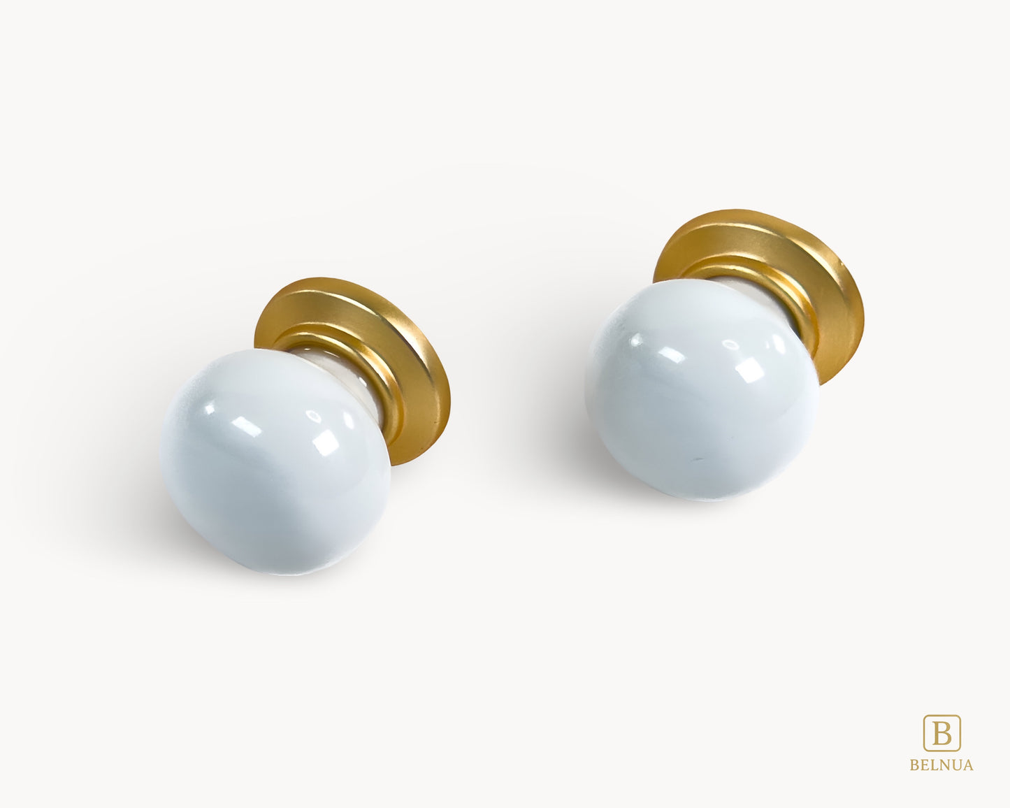 Front angled flat lay view of two Zerra white porcelain knobs with gold base | Belnua
