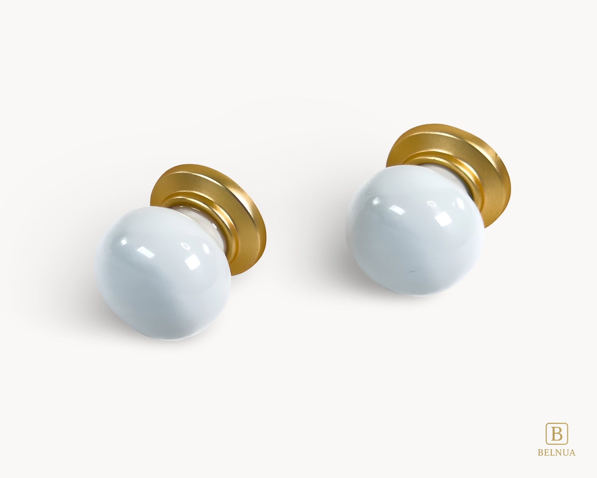Front angled flat lay view of two Zerra white porcelain knobs with gold base | Belnua