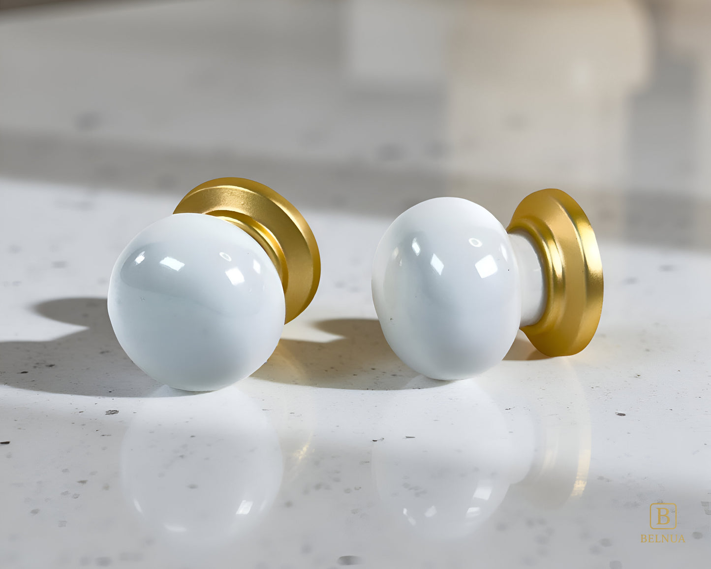 Two white spherical Zerra cabinet knobs with gold bases on a quartz surface | Belnua