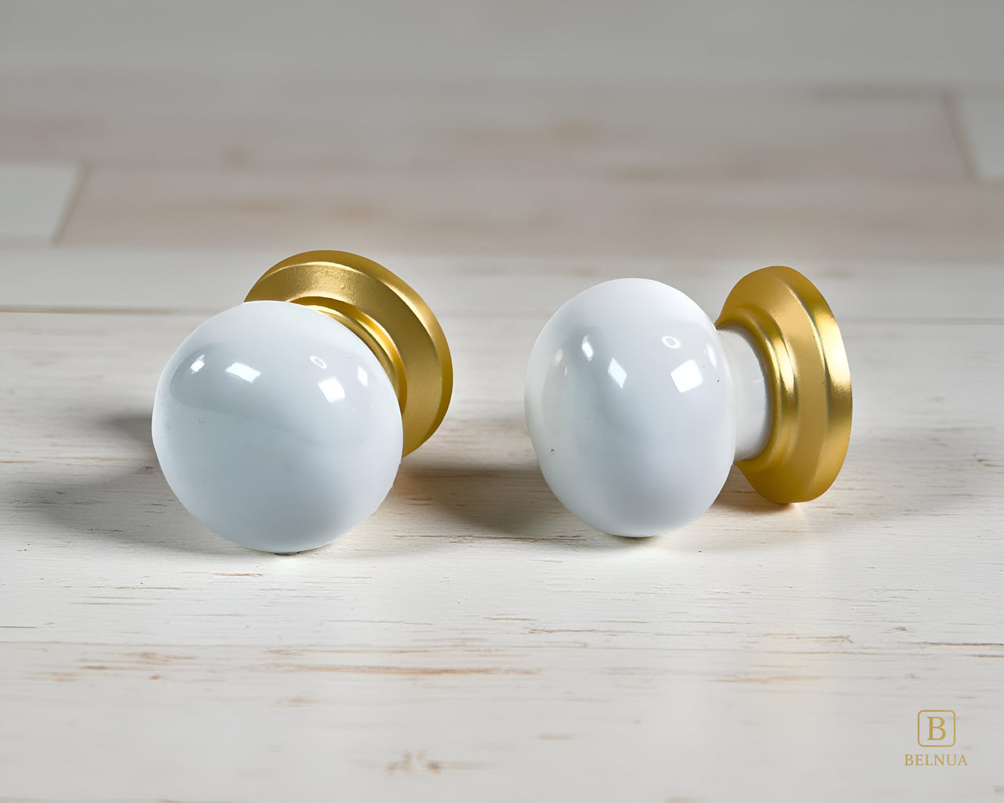 Two white Zerra porcelain knobs with gold accents on a wooden surface | Belnua