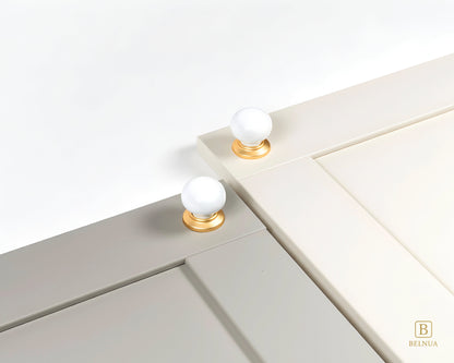 Close-up of a stone grey and cashmere cabinet doors with Zerra white ceramic knobs and gold bases | Belnua