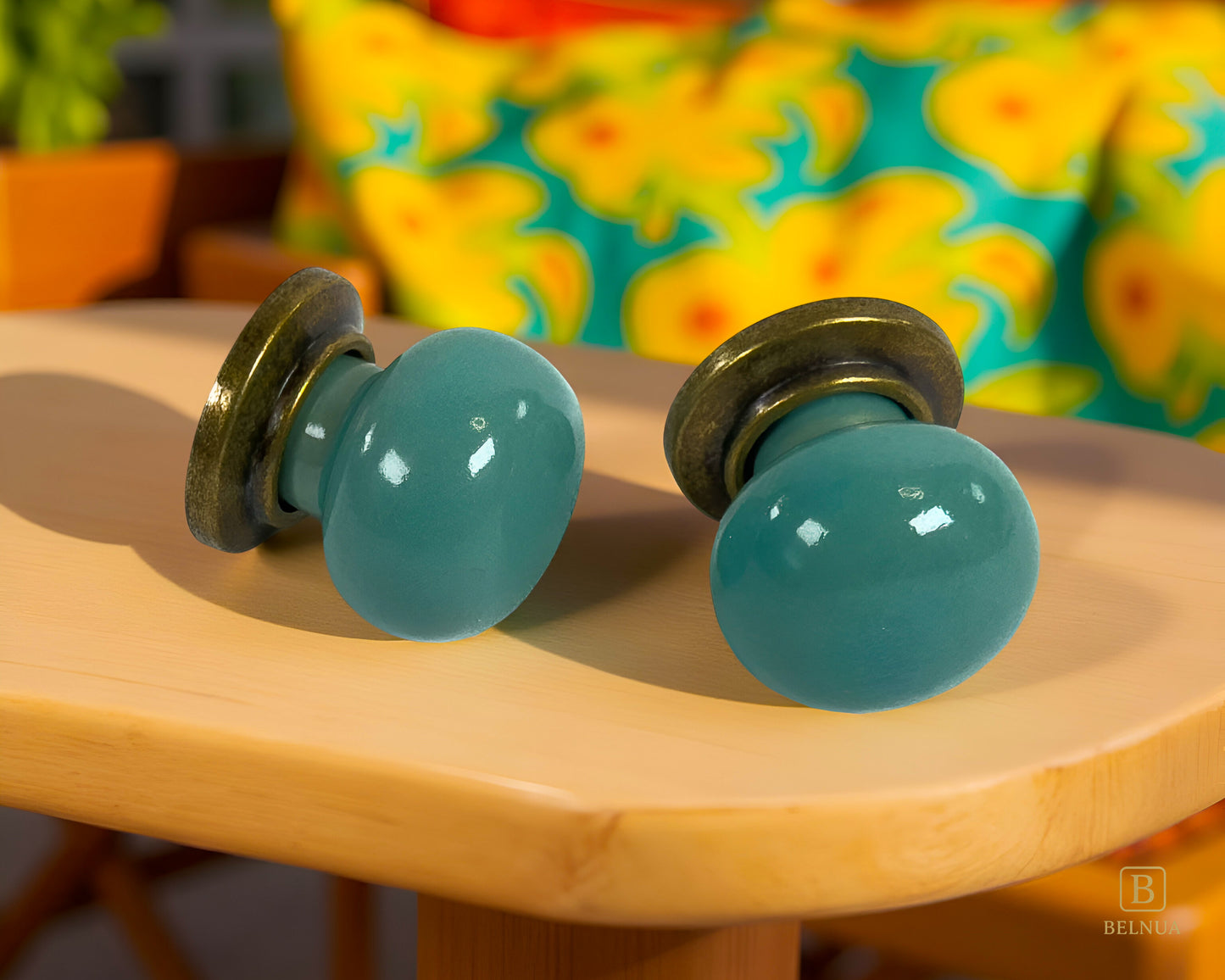Pair of Zerra turquoise cabinet knobs on a wooden surface with a colorful floral pattern in the background | Belnua