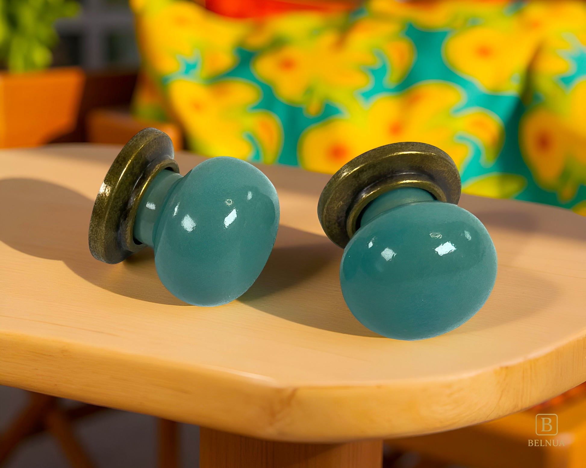 Pair of Zerra turquoise cabinet knobs on a wooden surface with a colorful floral pattern in the background | Belnua