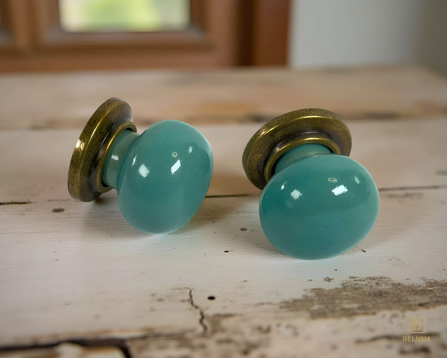 Pair of Zerra porcelain turquoise cabinet knobs with brass hardware on a wooden surface | Belnua
