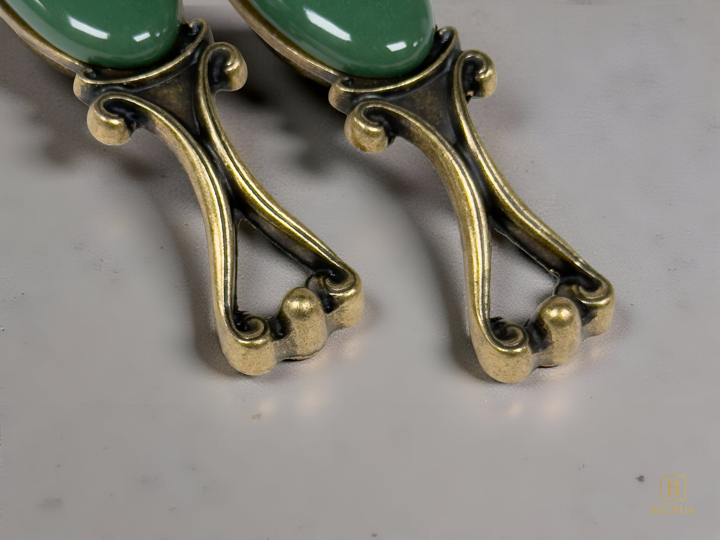 Belnua - Close up view Nureya decorative cabinet handles pair with dark green porcelain and brass base  on a grey surface
