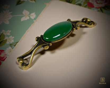Belnua - Left angled view of Nureya decorative cabinet handle with dark green porcelain and brass base  on a floral pattern surface