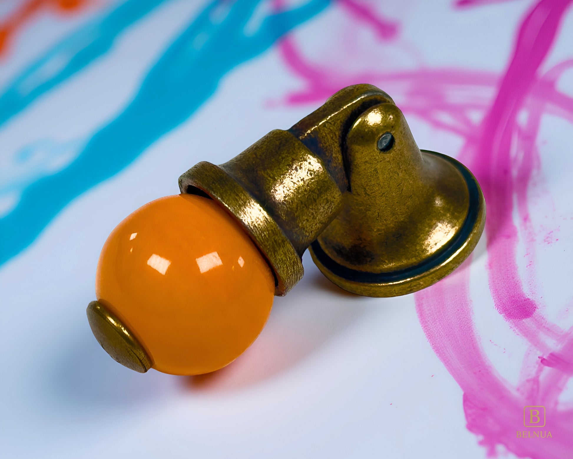 Belnua - Close-up of Virella orange porcelain insert and sculptural antique brass base on coloured splash surface