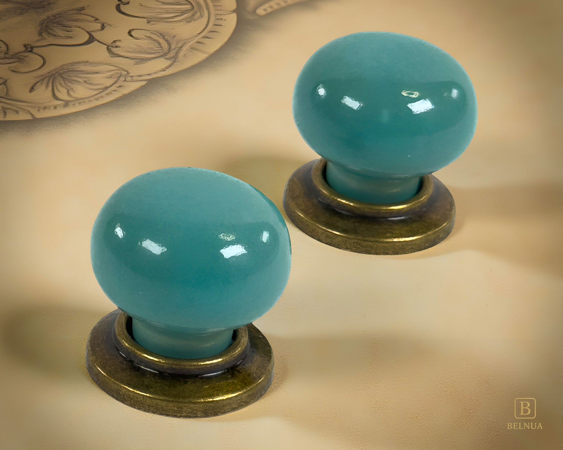 Pair of Zerra ceramic turquoise cabinet knobs with brass bases on a beige surface | Belnua