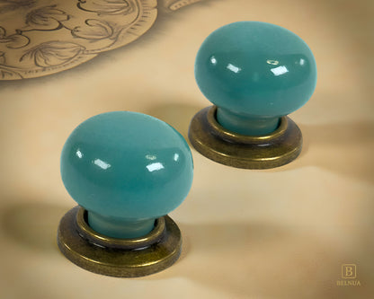 Pair of Zerra ceramic turquoise cabinet knobs with brass bases on a beige surface | Belnua