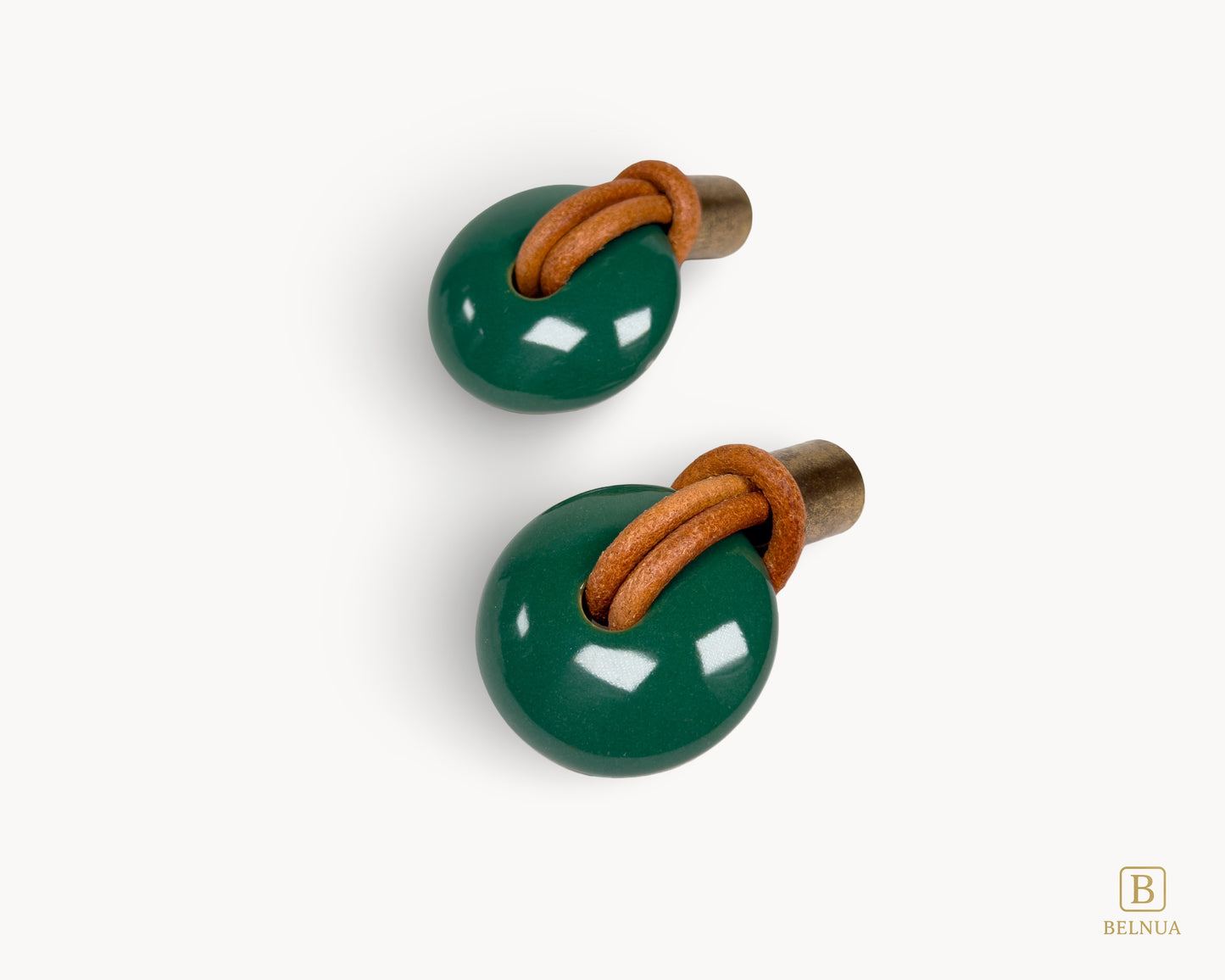Angled view of two green porcelain cabinet knobs featuring a weathered antique brass finish and tan leather straps.