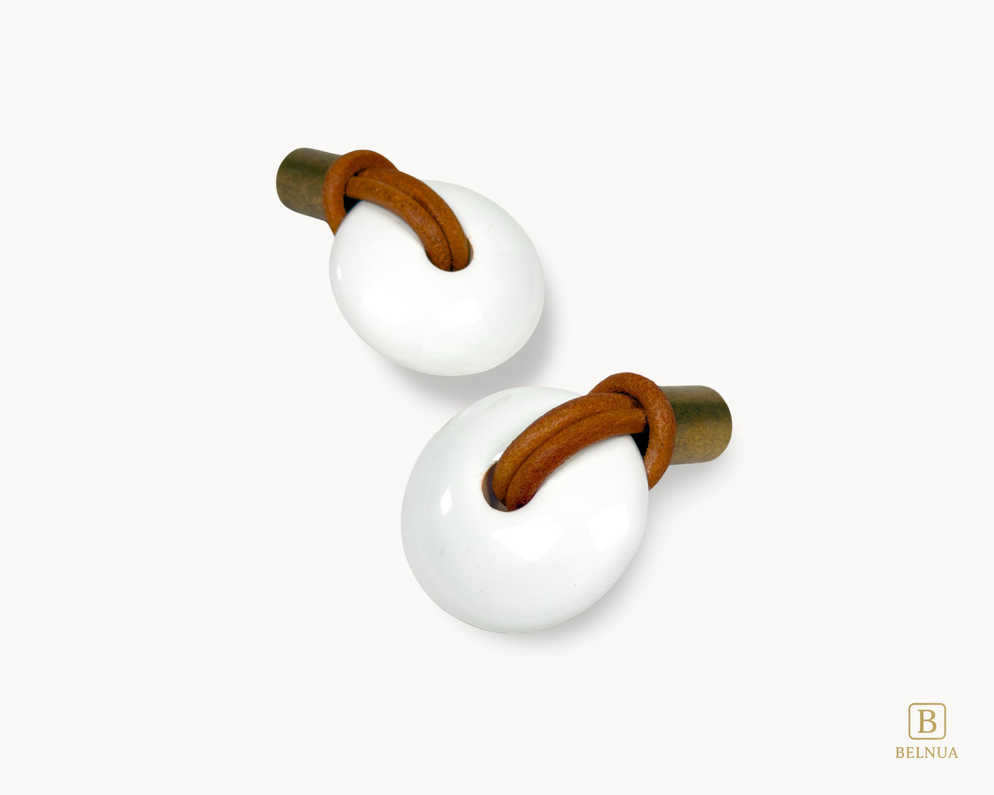 Overhead perspective of a pair of Belnua Revina knobs highlighting the antique brass finish and white porcelain curves.