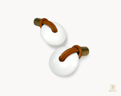 Overhead perspective of a pair of Belnua Revina knobs highlighting the antique brass finish and white porcelain curves.