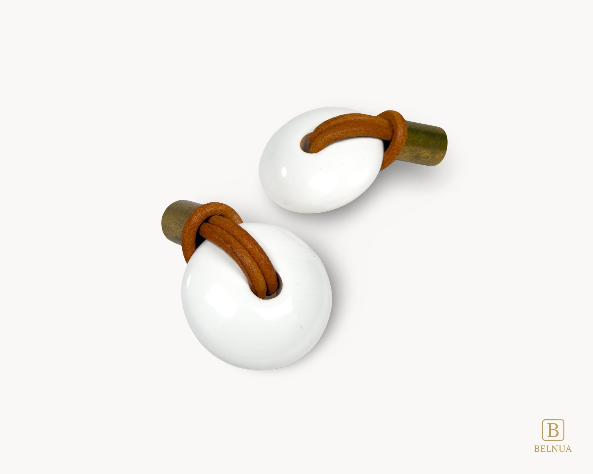 Two cabinet knobs showing the elegant combination of antique brass, white porcelain, and genuine leather.