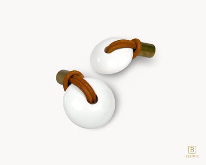 Two cabinet knobs showing the elegant combination of antique brass, white porcelain, and genuine leather.